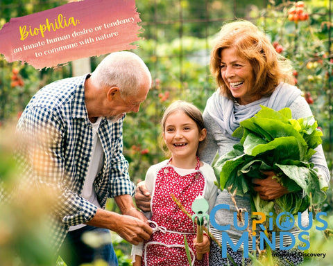 Two grandparents are gardening with their young granddaughter. They are laughing and smiling, while surrounded by homegrown fruit and vegetables. The image reads 'Biophilia; an innate human desire or tendency to commune with nature'.