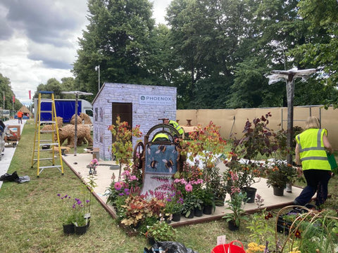 An outdoor exhibition being built containing flowers and Hug Rugs