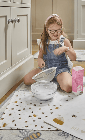 Girl playing with flour on top of bee tea towel