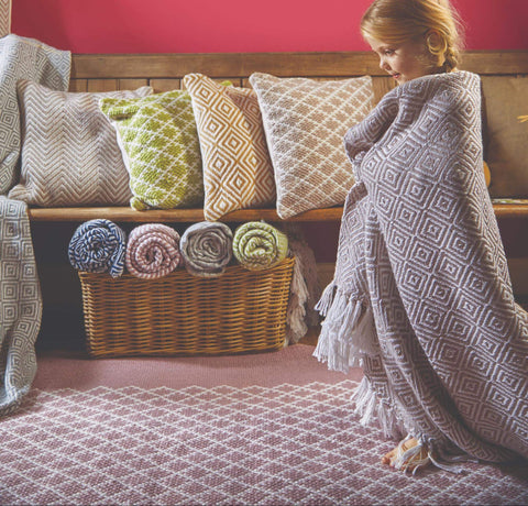 A young girl walking across a woven rug wrapped in a woven blanket