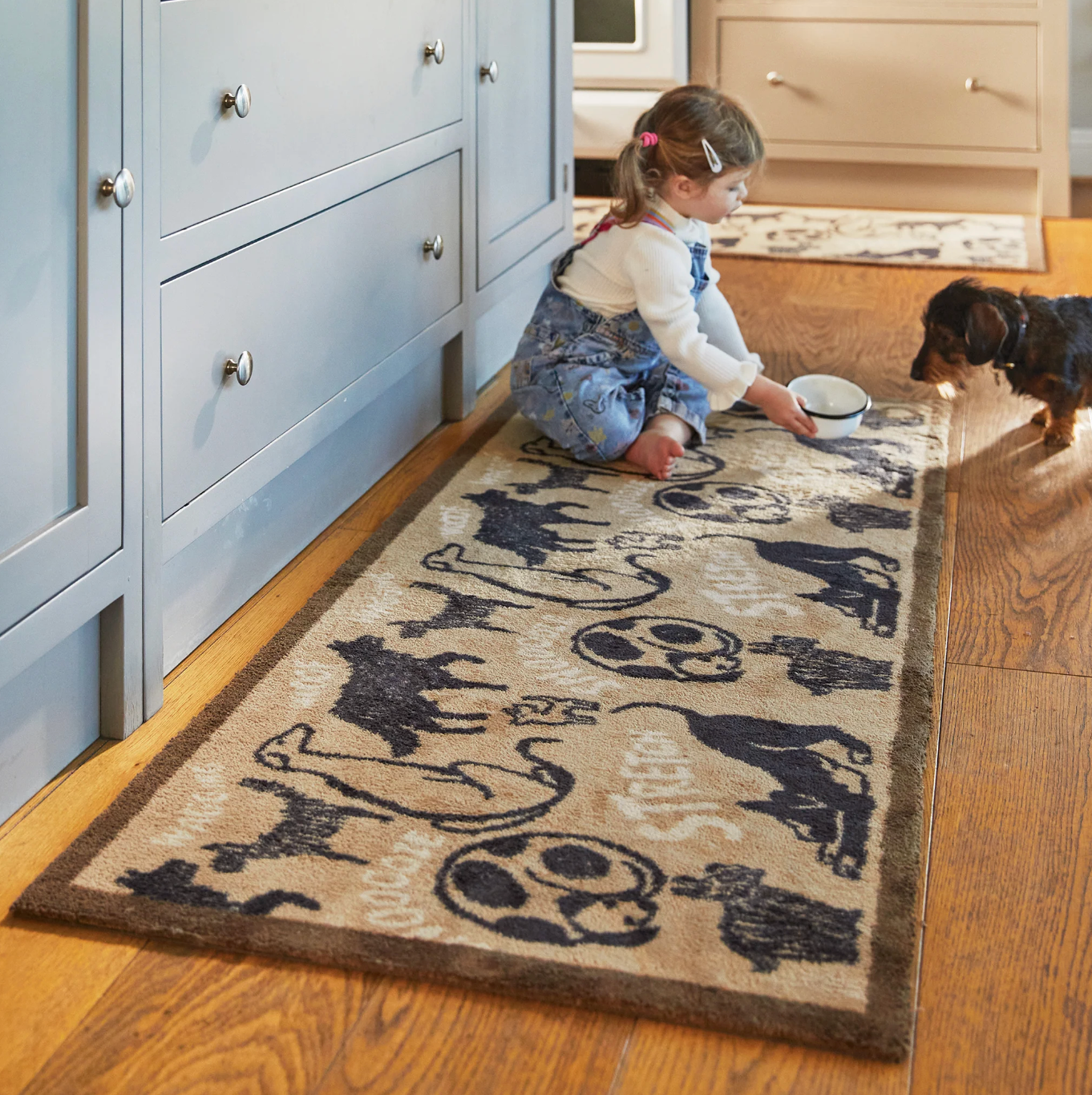 Young girl sat on a dog themed kitchen runner mat feeding a dog