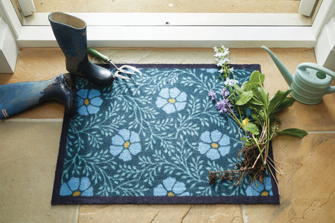 A blue floral front door rug with wellies and flowers on top 