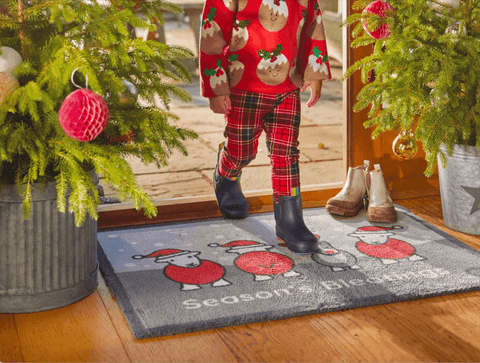 A child walking across a front door mat that has sheep with santa hats on