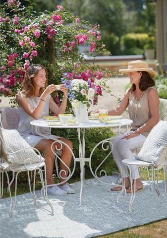 Women sat around a table talking in a garden on a blue rug