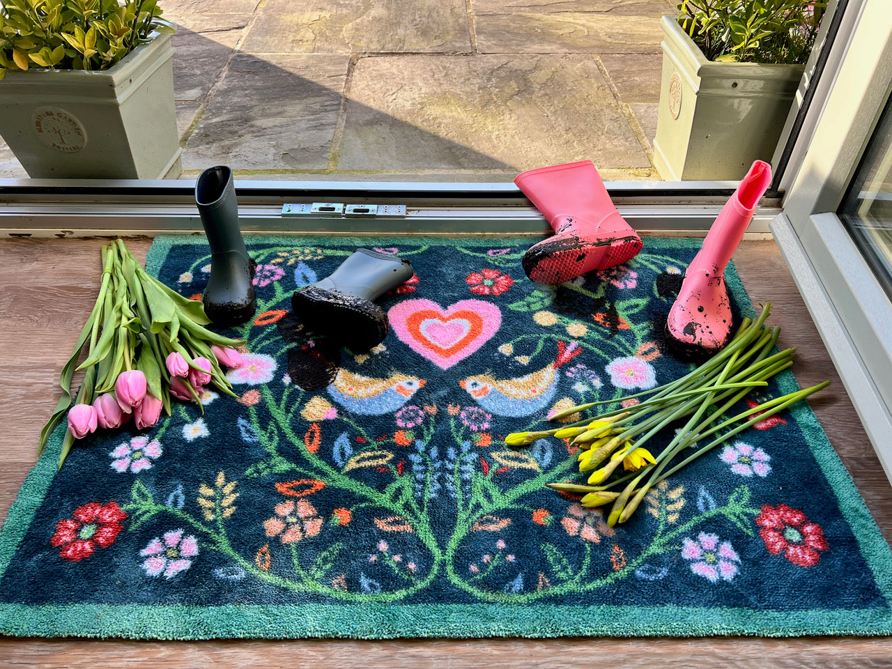 A floral door mat with flowers and wellies on top of it