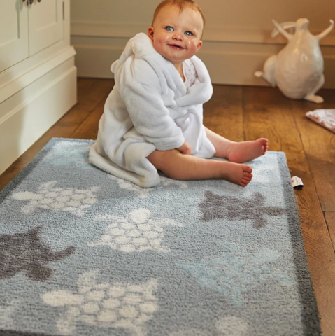 Baby sat on a rug with sea turtles on it