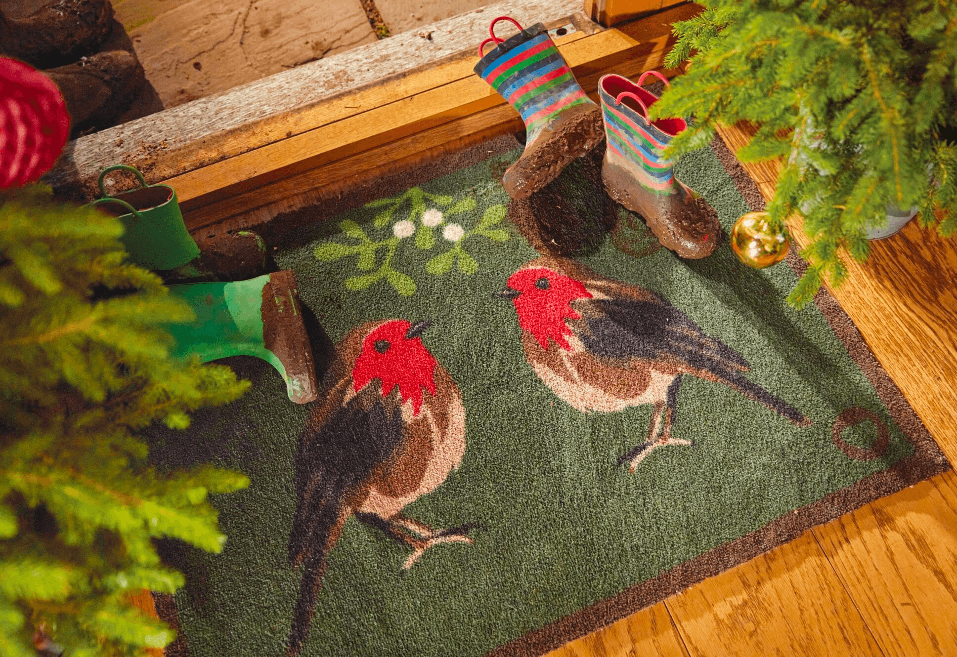 A green front door mat with a drawing of two robins on surrounded by muddy wellies