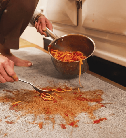 Someone picking spaghetti off a grey kitchen floor runner