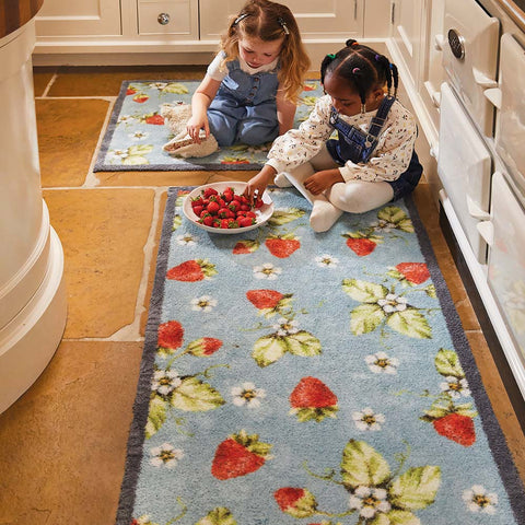 Two girls eating a bowl of strawberries on a strawberry design rug