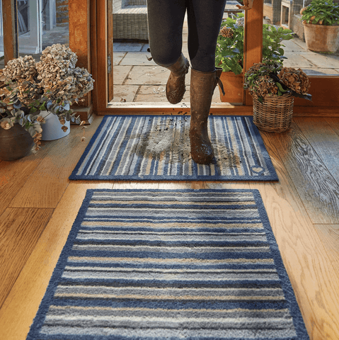 Someone walking on a striped front door mat in muddy wellies