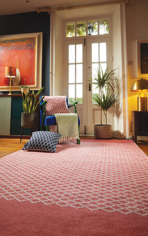 A woven pink rug in a living room with colourful cushions and throws on a sofa