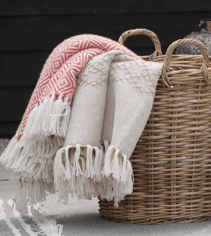 A woven basket with two woven throws folded over the side