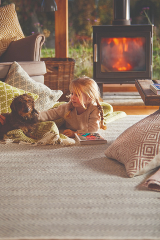 a young girl and dog lying on a woven rug in front of the fire