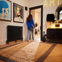 A woman walking across a large jute rug in a hallway