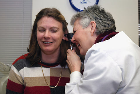 A woman in her mid-30s sitting in the examination chair for an ear examination by an otolaryngologist
