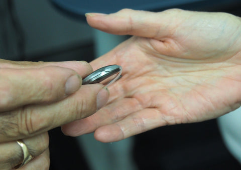 A man with a ring on his finger is handing a hearing aid to another person