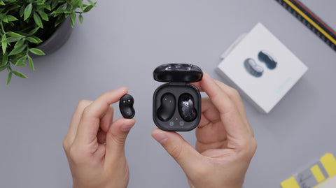 Two hands are holding black ear buds in the case