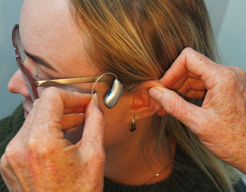 a blonde woman is wearing behind the ear hearing aids