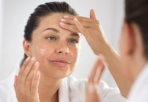 Model applies cream to face in mirror.