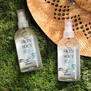 Two large bottles of Skin So Soft dry oil lie on the background of grass and a summer hat.