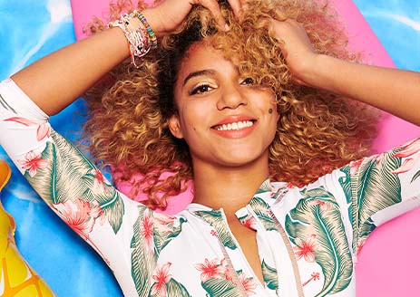 Model with curly hair lies on summer floor background in tropical top with bracelets.