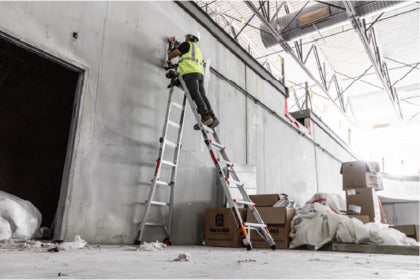 A man on a multi-position ladder in an unfinished building, working on construction.