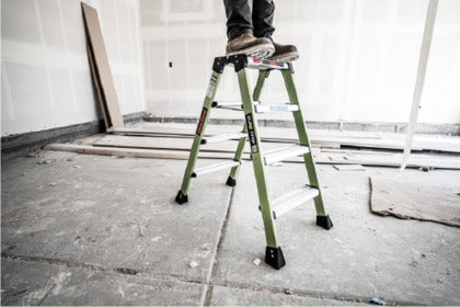 Man using a step stool to reach higher on a ladder indoors.