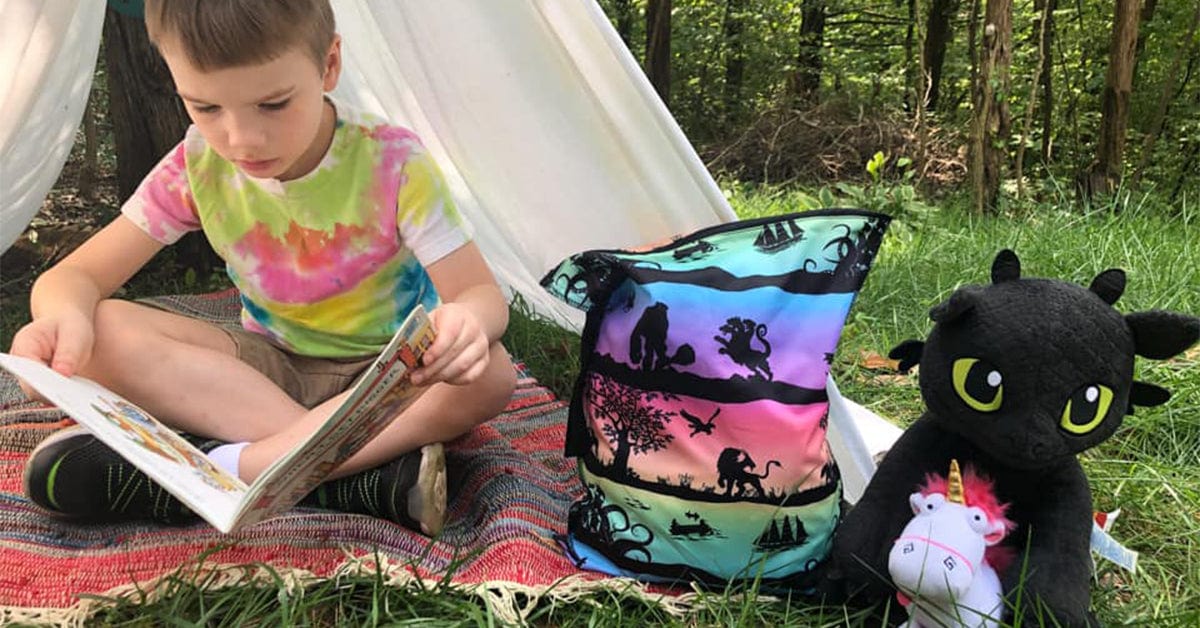 boy outside in a tent reading with a dragon
