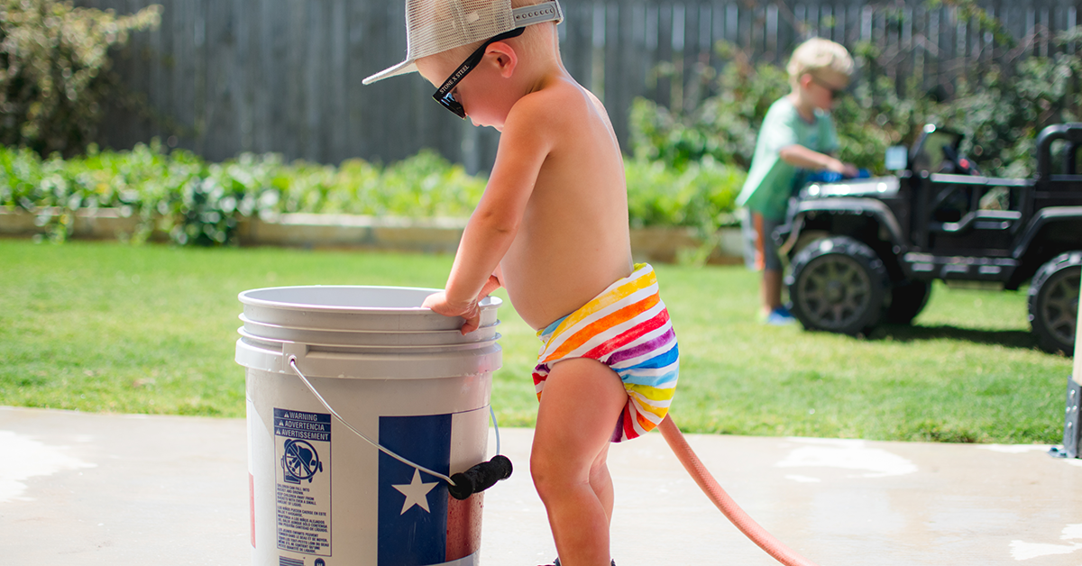 baby wearing cloth diaper next to bucket for stripping cloth diapers