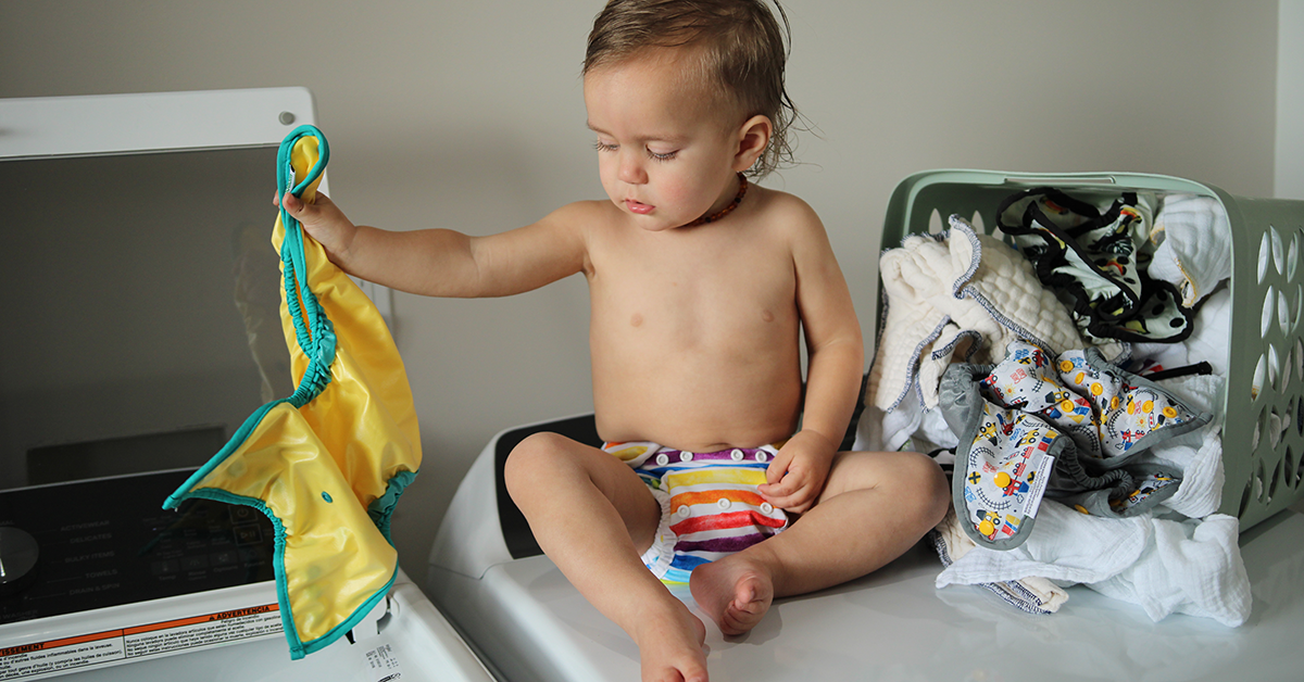 baby throwing cloth diaper in washing machine for cloth diaper stripping