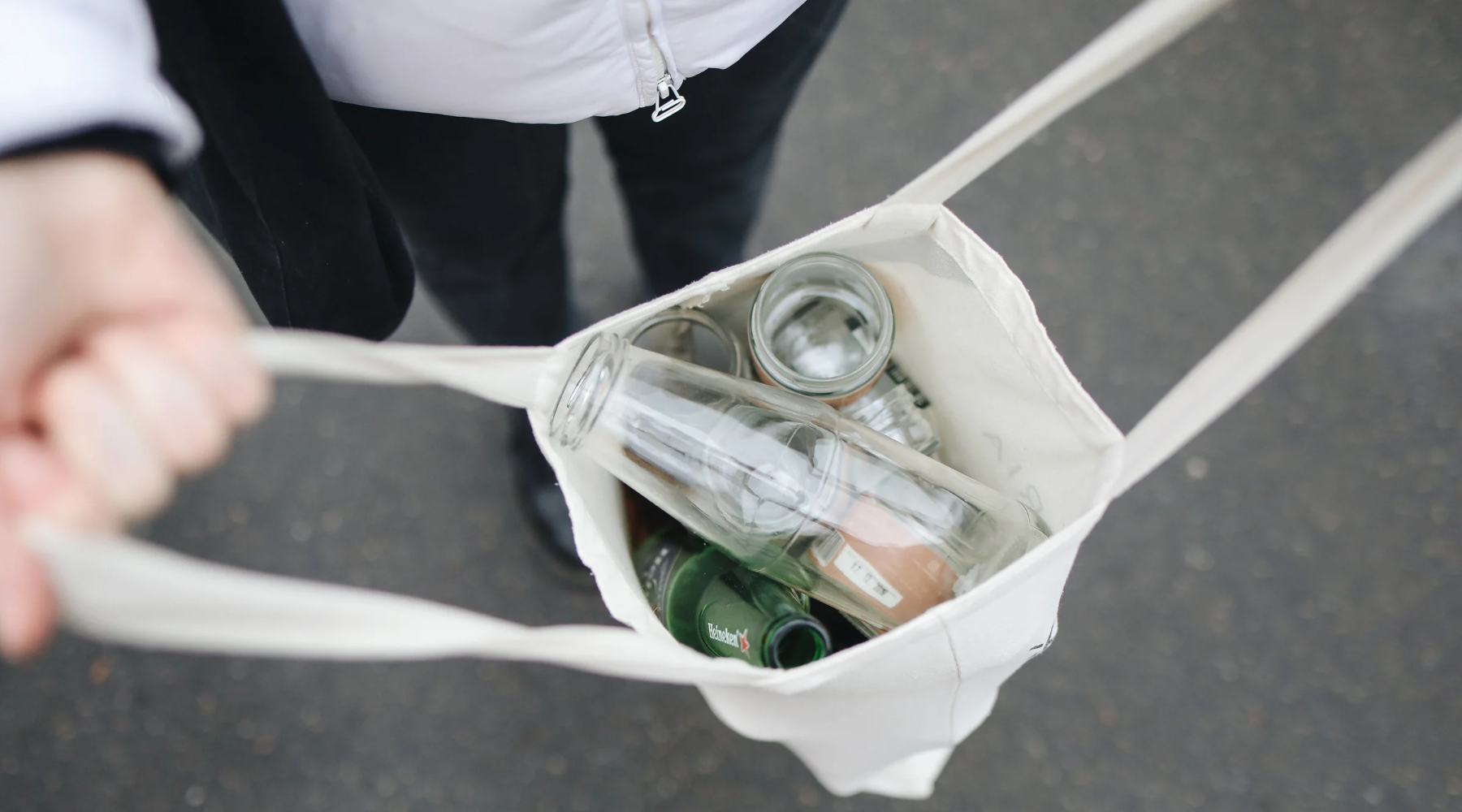 A reusable tote bag with empty glass bottles inside.