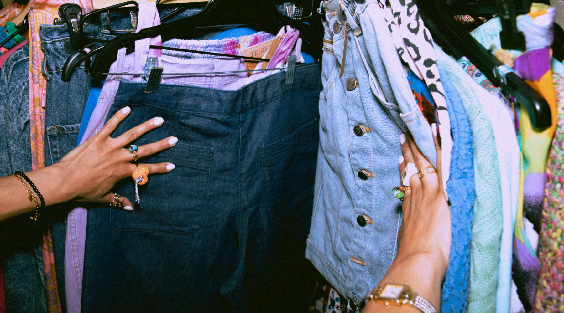 Someone browsing through a clothing rack from their point of view. They are wearing lots of rings and bracelets.