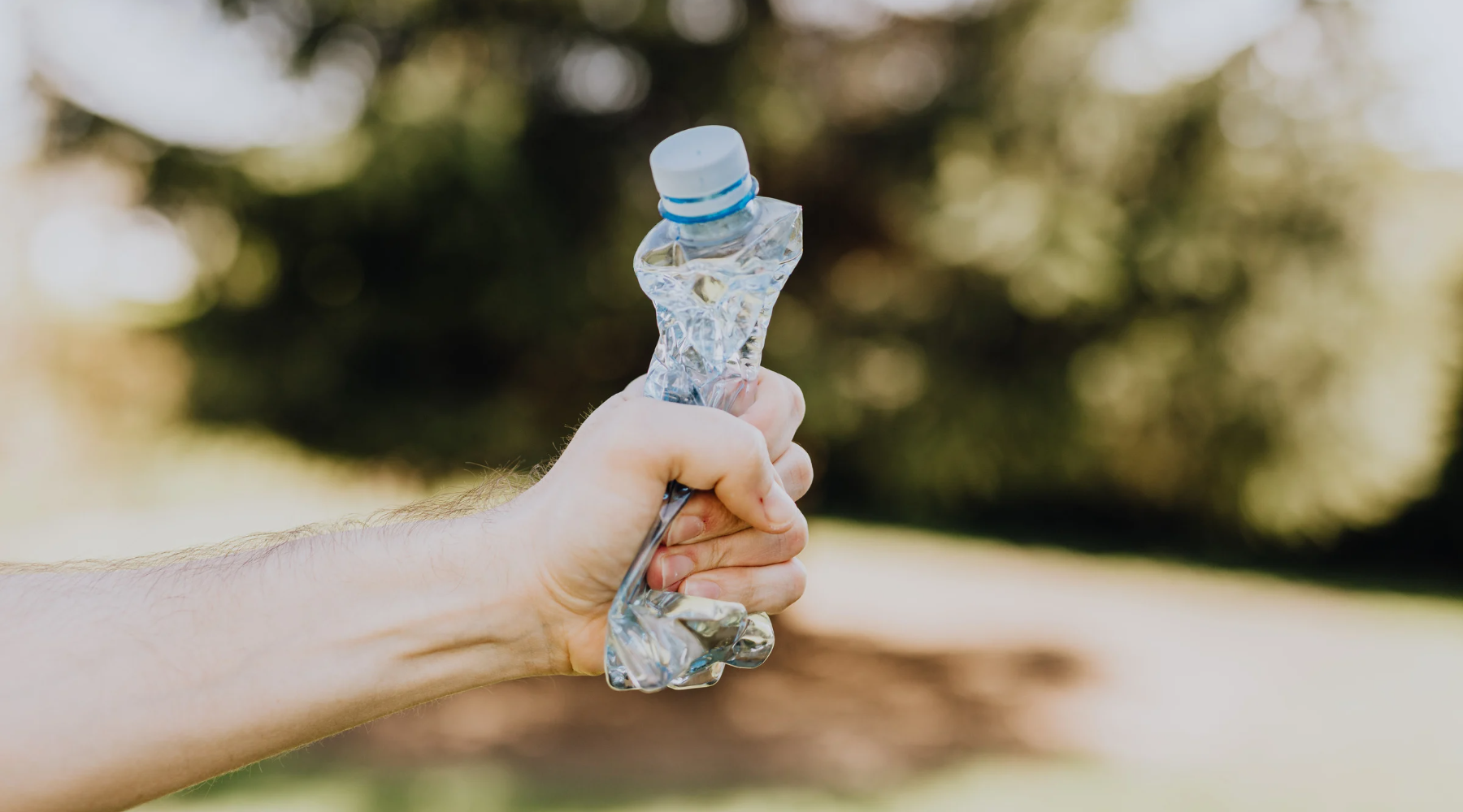 A hand forcefully squeezing an empty plastic water bottle.