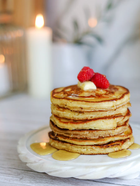 Fluffy stack of buttermilk pancakes topped with butter, maple syrup, and raspberries