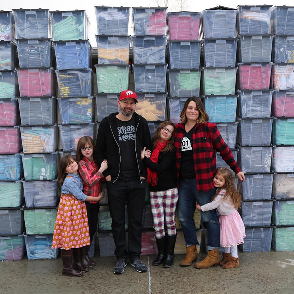 Stately Type founders David and Holly Lesue (and kids) standing in front of rows of bins holding inventory