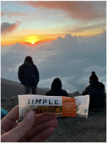 hikers on top of mountain above clouds watching sunset and holding a simple bar