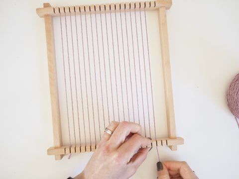 finishing off warping a wooden weaving loom with purple cotton warp string