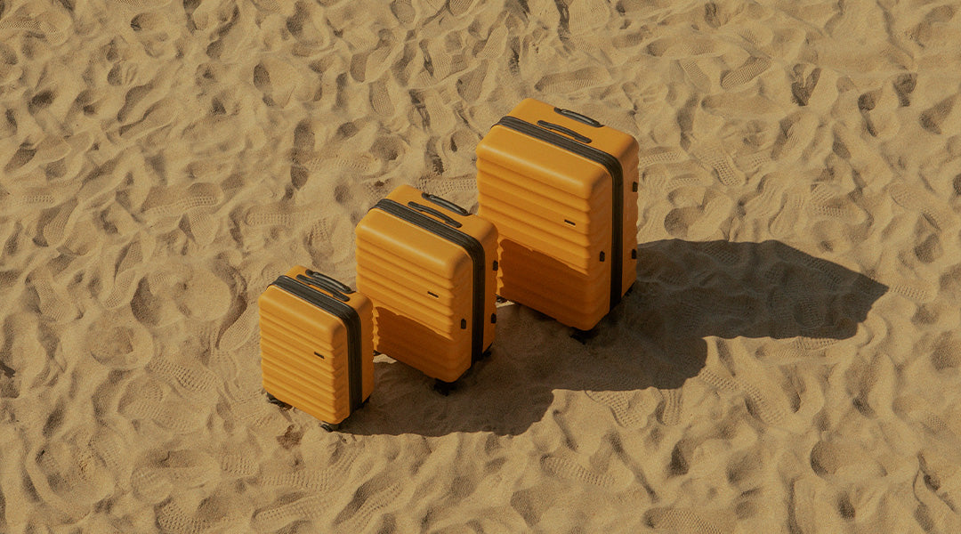 Antler Clifton suitcases set of three in Ochre yellow on beach 