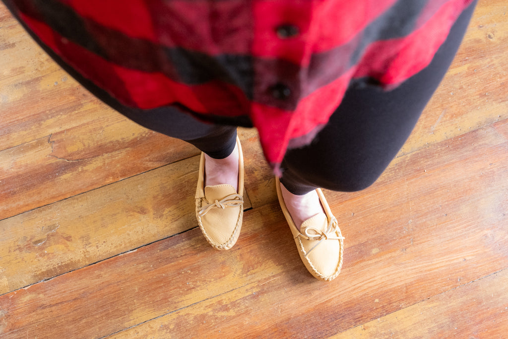 Woman wearing light tan colored moccasins slippers with buffalo plaid shirt