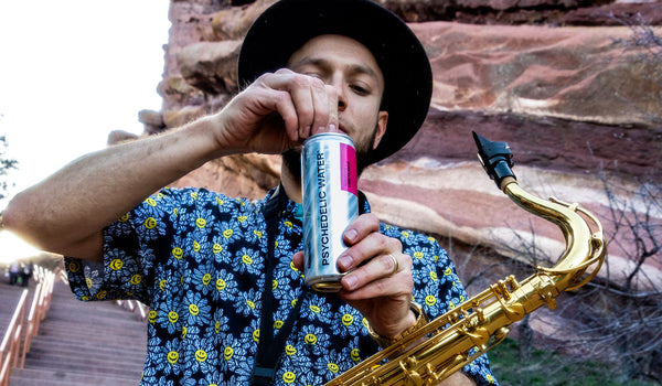 Multi-intrumentalist Brandon Theis, aka The Orchestrator, with saxophone, opening can of Psychedelic Water