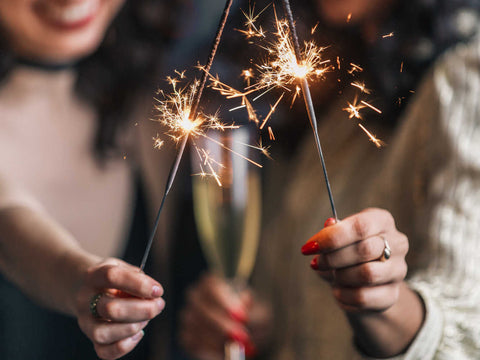 hands holding two lit sparklers with a glass of champagne