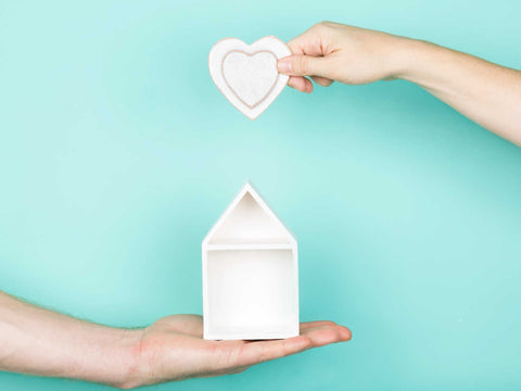 hands holding wooden heart over small house