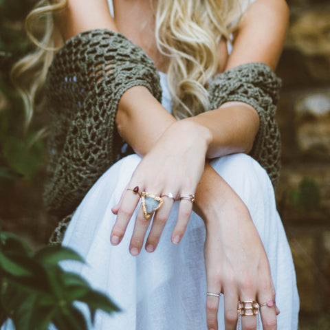 Woman in white dress and grey shawl sitting wearing rings on her fingers