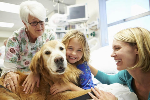 Little girl hugging a therapy dog, with her mother by her side.