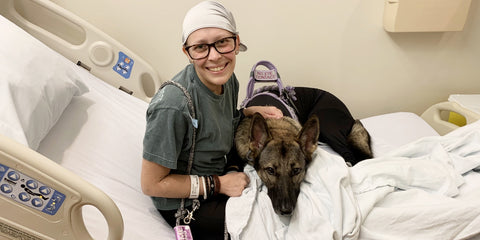 Smiling woman in a hospital bed with a therapy dog. 