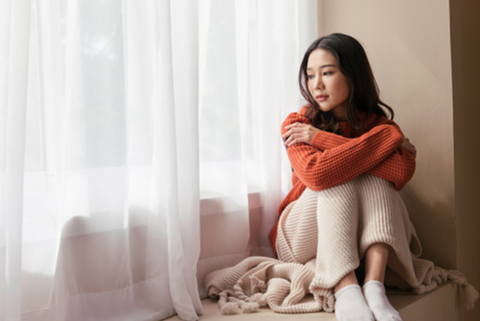 A sad woman sitting in front a window.