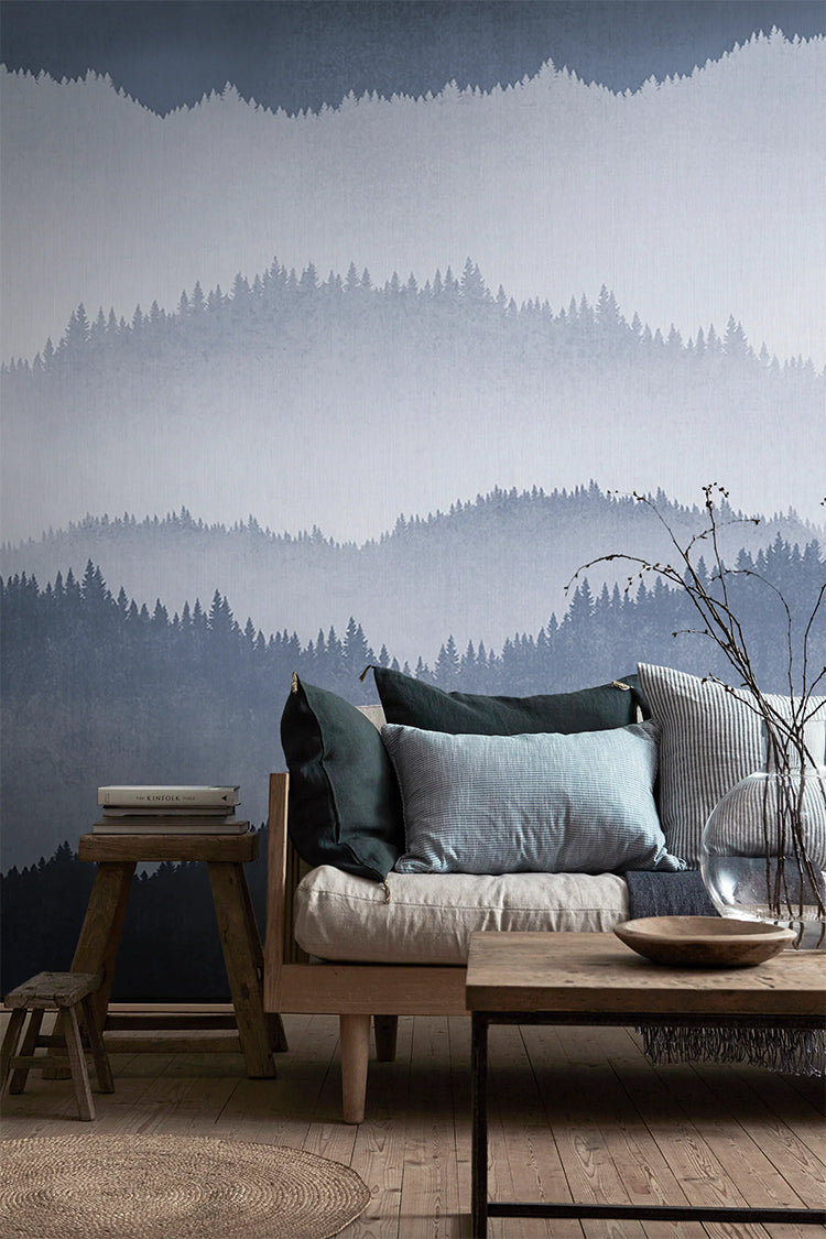 Forest Landscape, Ombre Mural Wallpaper in Dark Blue featured in a wall of a living area with wooden furnitures and flooring, with an assortment of pillows on top of a cushion.