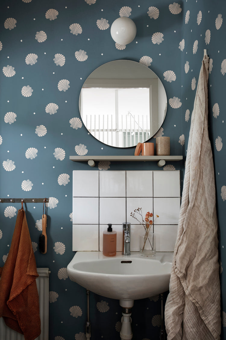 Picking Seashells, Wallpaper in Blue Featured on a wall of a toilet, with a round mirror and a lavatory with several products on top of it