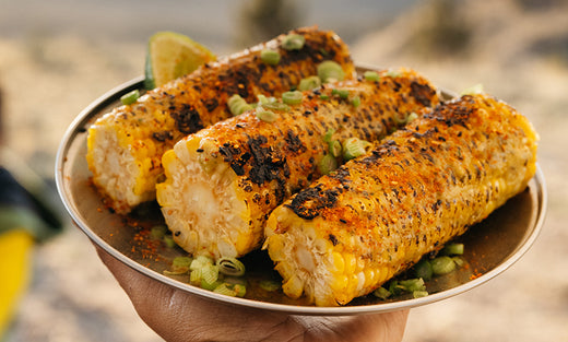 Three ears of grilled corn on the cob, topped with miso butter, scallions, and lime all resting on a Titanium Plate.