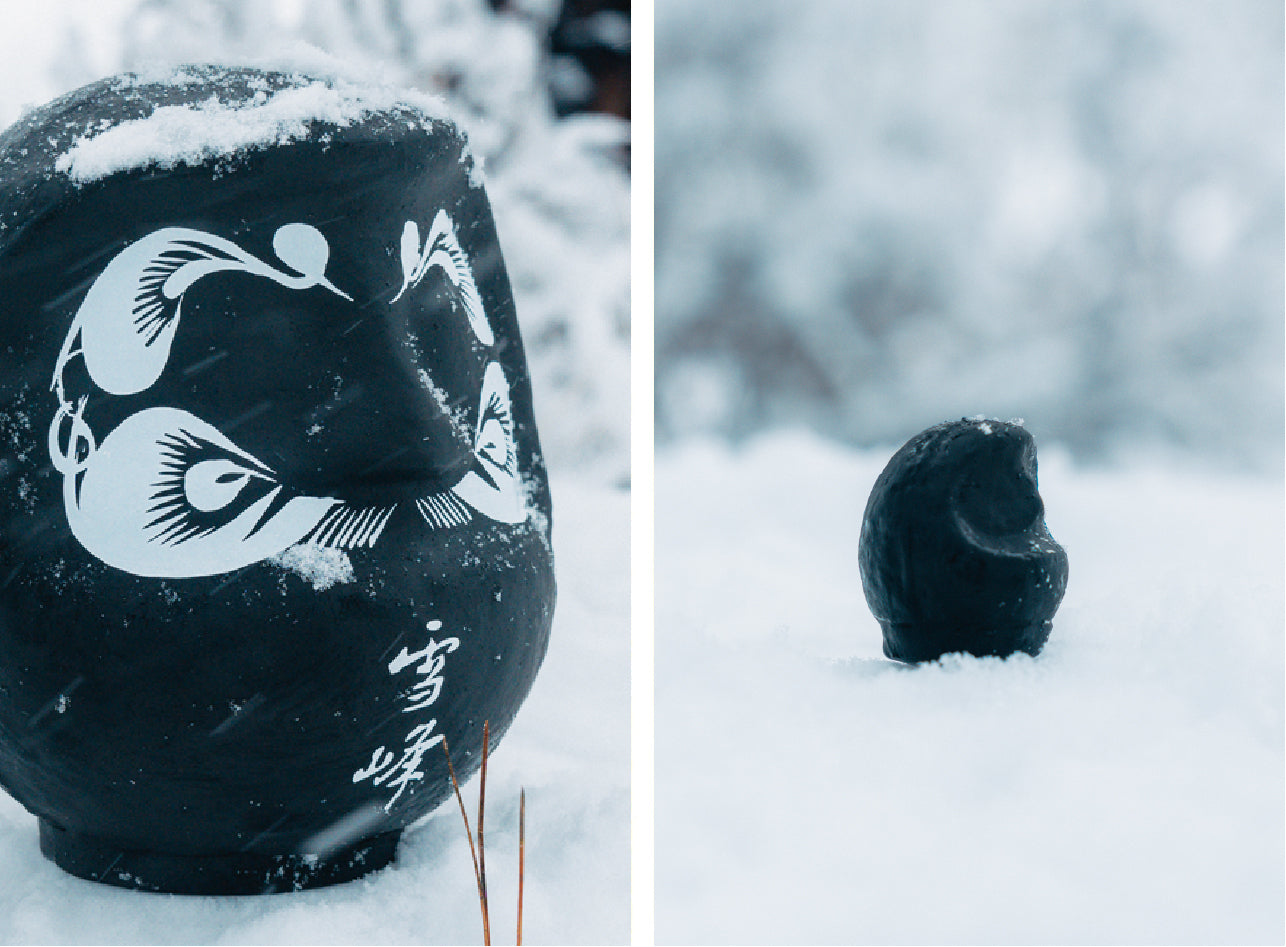 A side by side image of a large and small black Daruma doll